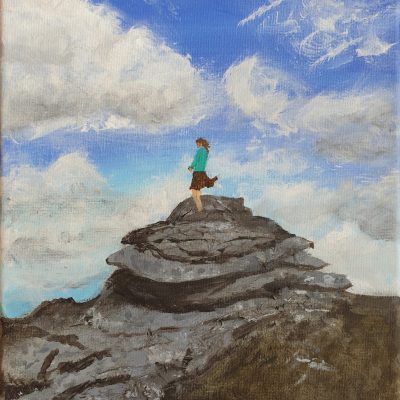 A self-portrait of Anita Daffern climbing on stacked rocks in Dartmoor. The sky is visible behind, blue with puffy clouds.