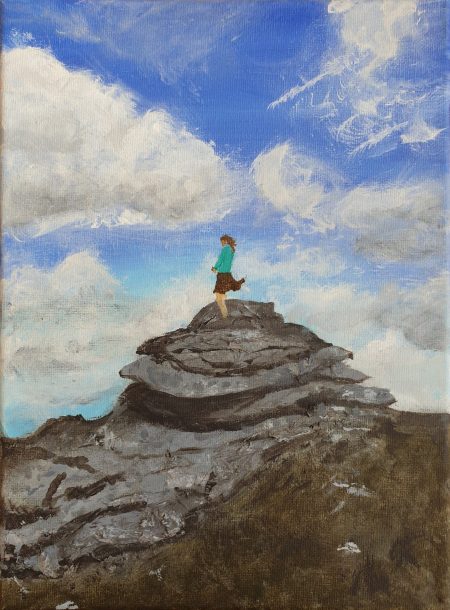 A self-portrait of Anita Daffern climbing on stacked rocks in Dartmoor. The sky is visible behind, blue with puffy clouds.